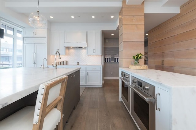 kitchen with paneled refrigerator, white cabinetry, hanging light fixtures, and stainless steel oven