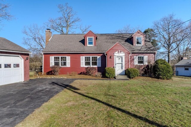 cape cod home featuring driveway, roof with shingles, a front yard, a garage, and a chimney