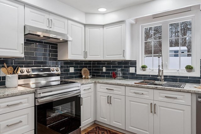 kitchen with under cabinet range hood, stainless steel electric range oven, plenty of natural light, and decorative backsplash