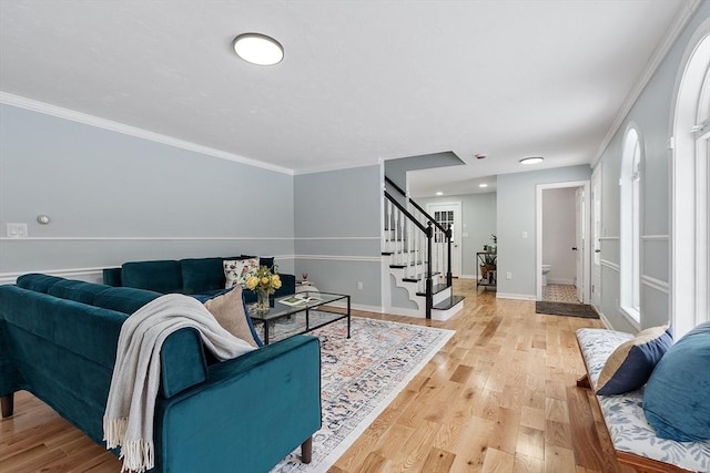 living area featuring stairs, light wood-style floors, baseboards, and ornamental molding