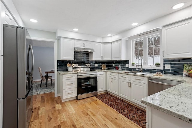 kitchen with light wood-style flooring, under cabinet range hood, a sink, appliances with stainless steel finishes, and white cabinets