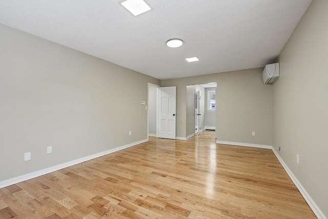 empty room featuring baseboards, light wood finished floors, and a wall unit AC