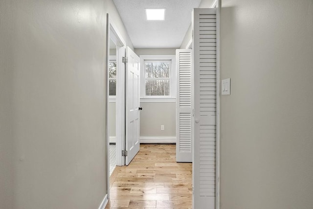 hallway featuring light wood-style floors, baseboards, and a textured ceiling