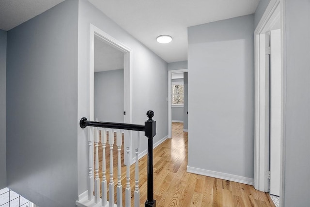 corridor with light wood-style flooring, an upstairs landing, and baseboards