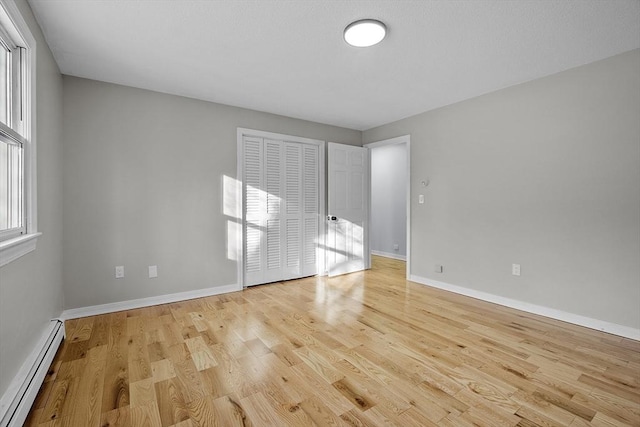 unfurnished bedroom with a closet, baseboards, baseboard heating, and wood finished floors