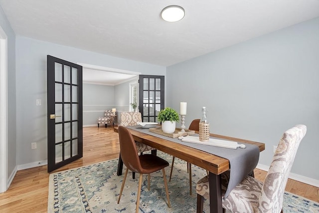 dining space with french doors, baseboards, and light wood finished floors