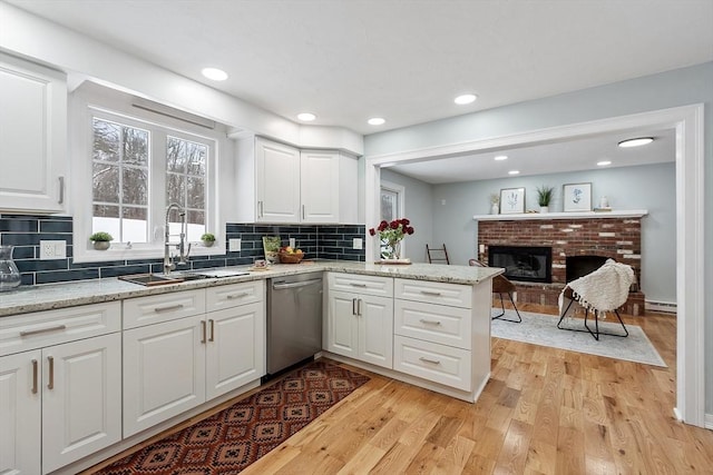 kitchen featuring light wood finished floors, dishwasher, a fireplace, white cabinets, and a sink