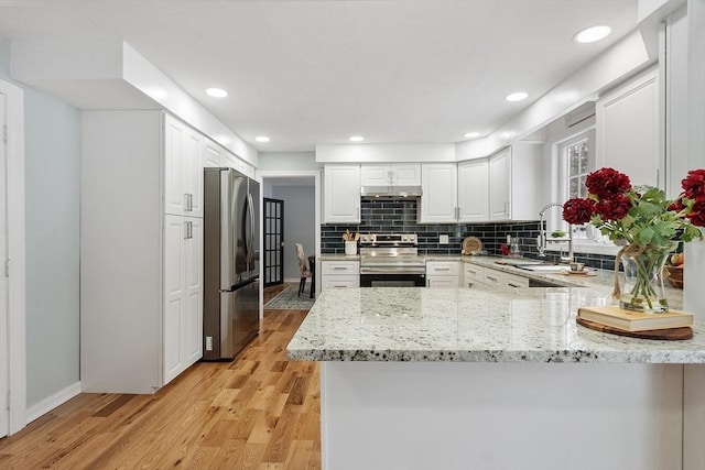 kitchen with a sink, under cabinet range hood, light wood-style floors, appliances with stainless steel finishes, and a peninsula