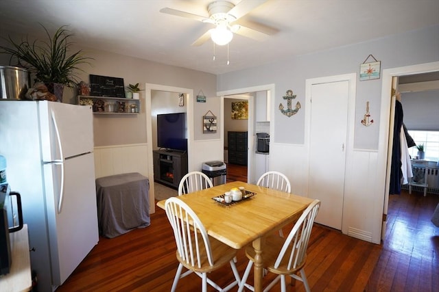 dining room featuring ceiling fan, hardwood / wood-style floors, wainscoting, and a fireplace