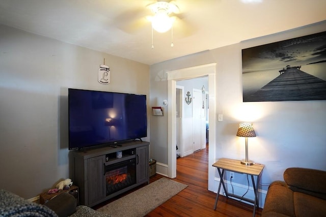 living area featuring dark wood finished floors, a ceiling fan, and baseboards