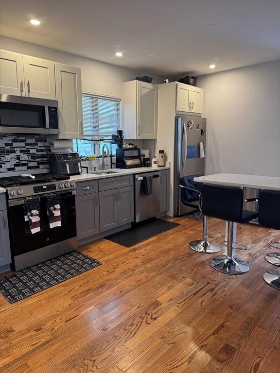 kitchen with gray cabinets, tasteful backsplash, sink, stainless steel appliances, and light wood-type flooring