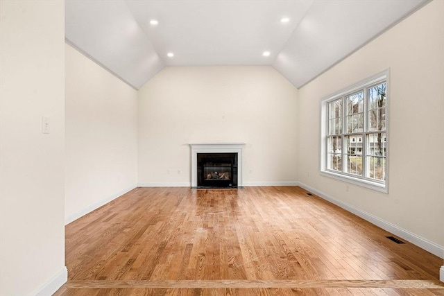 unfurnished living room featuring visible vents, baseboards, light wood-style flooring, a fireplace with flush hearth, and vaulted ceiling