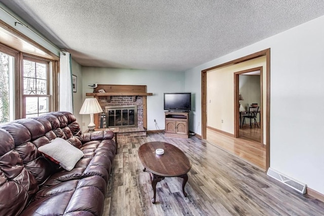 49 Lady Slipper Dr, Dennis, MA 02638 - living room featuring visible vents, a brick fireplace, wood finished floors, baseboards, and a textured ceiling