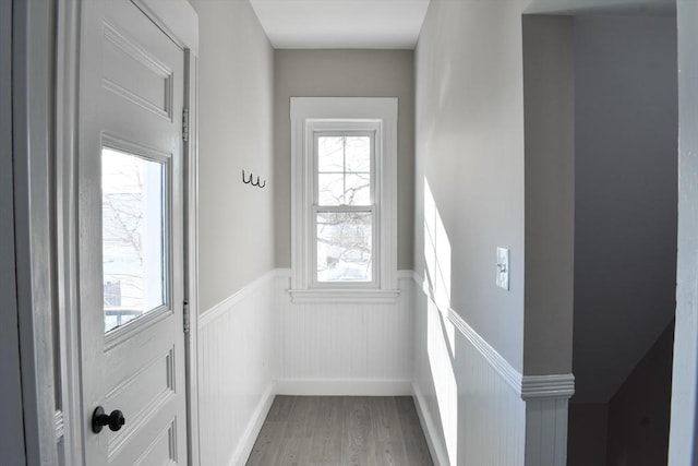 doorway to outside with light wood-type flooring and wainscoting