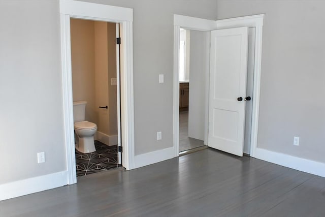 unfurnished bedroom featuring ensuite bath, baseboards, and wood finished floors