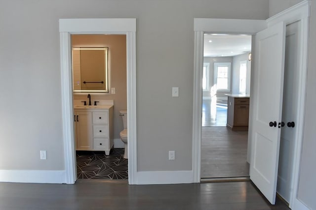 unfurnished bedroom with wood finished floors, ensuite bath, a sink, and baseboards