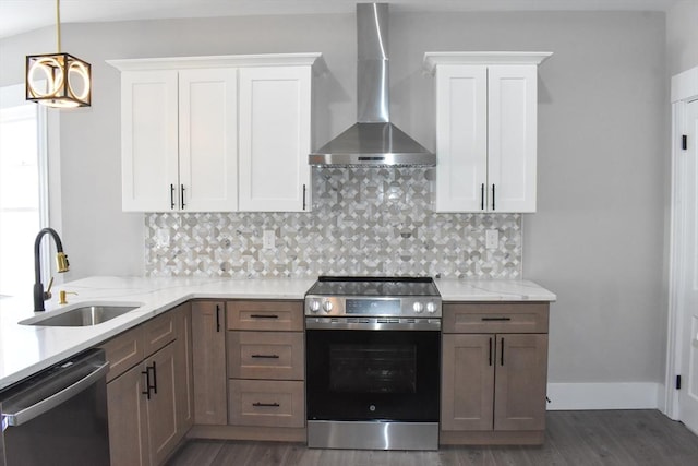 kitchen with decorative backsplash, appliances with stainless steel finishes, white cabinets, a sink, and wall chimney exhaust hood