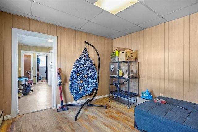 workout area with a paneled ceiling, wood-type flooring, baseboard heating, and wooden walls