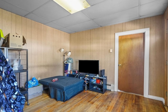 bedroom featuring baseboard heating, a paneled ceiling, wood walls, and hardwood / wood-style floors