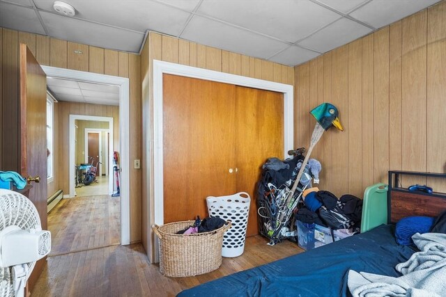 bedroom with hardwood / wood-style floors, a closet, a baseboard heating unit, and wood walls