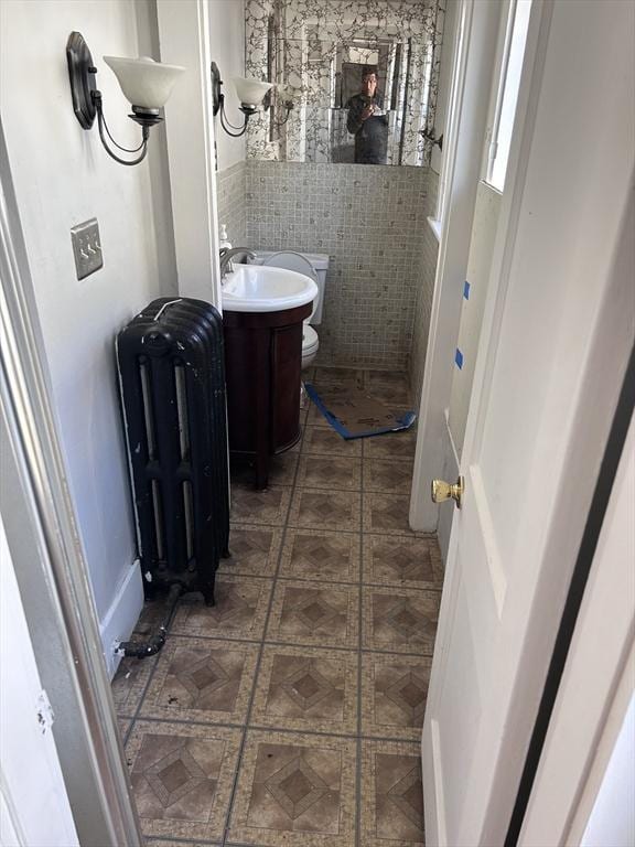 bathroom featuring radiator, tile patterned floors, toilet, vanity, and tile walls