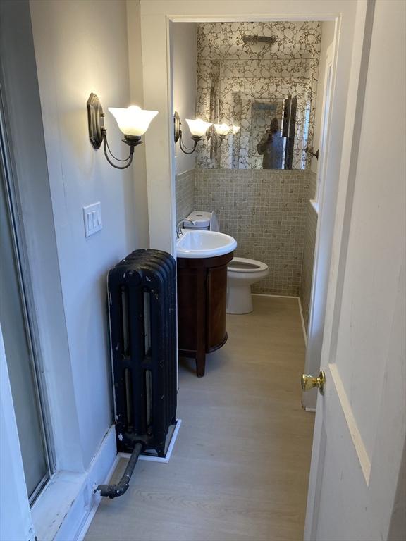 bathroom with vanity, radiator, hardwood / wood-style flooring, toilet, and brick wall