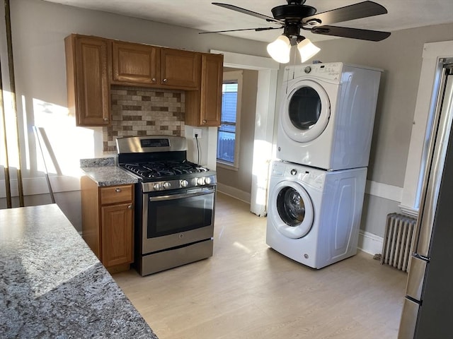 kitchen featuring decorative backsplash, radiator, stainless steel gas range oven, light hardwood / wood-style flooring, and stacked washer and dryer