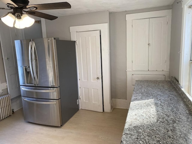 kitchen with stainless steel refrigerator with ice dispenser, light wood-type flooring, radiator, ceiling fan, and stone counters