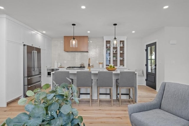 kitchen with a breakfast bar, high end fridge, white cabinetry, decorative light fixtures, and an island with sink