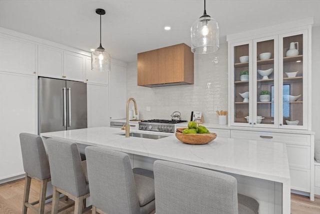 kitchen featuring decorative light fixtures, white cabinetry, high end refrigerator, light stone countertops, and a center island with sink