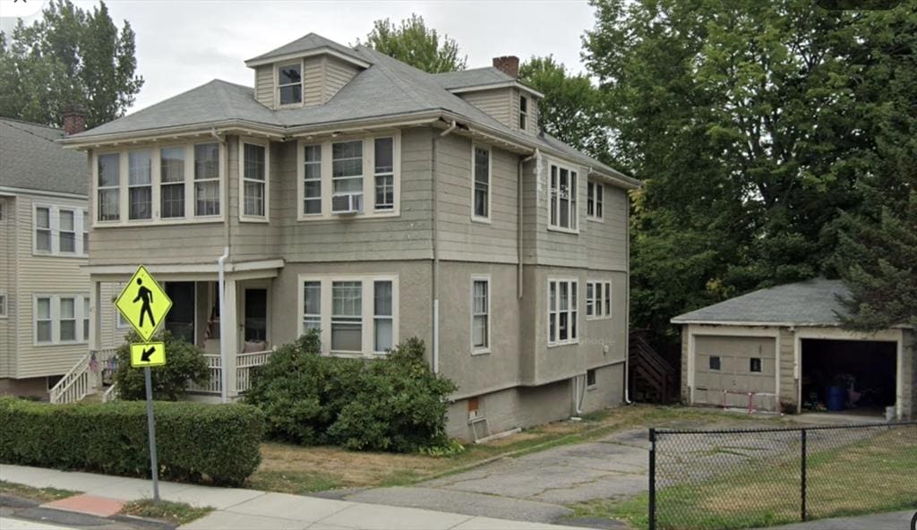 view of front facade featuring a detached garage, fence, stucco siding, a chimney, and an outbuilding