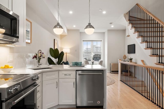kitchen featuring stainless steel appliances, a peninsula, a sink, light wood-style floors, and recessed lighting