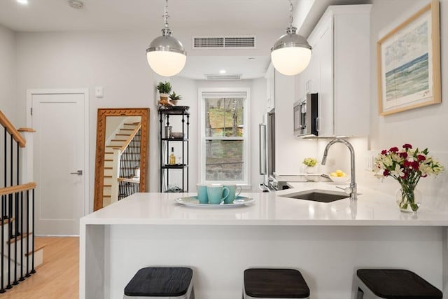 kitchen with a sink, stainless steel appliances, a peninsula, light countertops, and a breakfast bar area