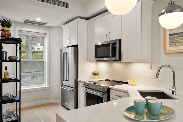 kitchen featuring appliances with stainless steel finishes, a sink, light countertops, white cabinetry, and light wood-style flooring