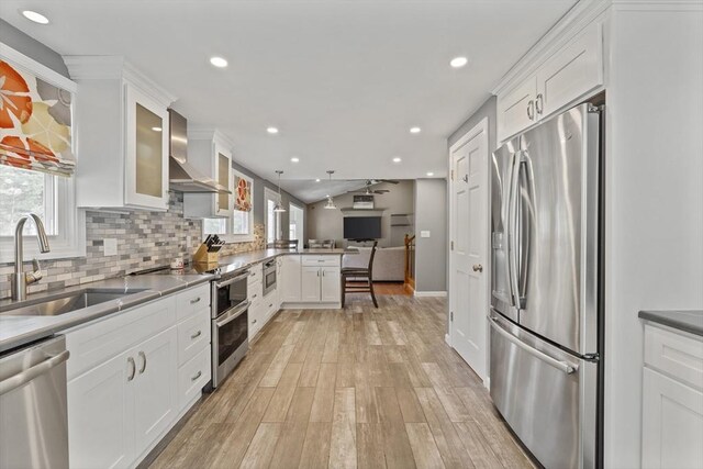 kitchen featuring a peninsula, a sink, appliances with stainless steel finishes, wall chimney exhaust hood, and open floor plan