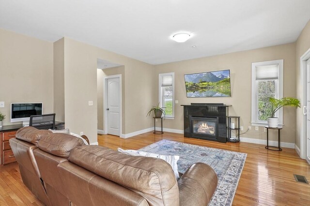 living area with baseboards, a glass covered fireplace, visible vents, and light wood-type flooring