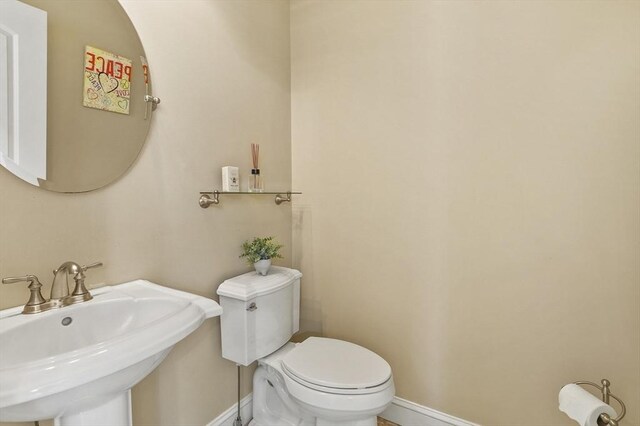 half bathroom with toilet, baseboards, and a sink