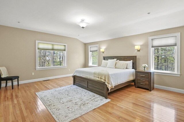bedroom with baseboards, vaulted ceiling, and light wood-style flooring