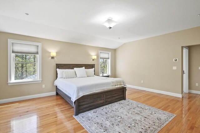 bedroom featuring baseboards, light wood finished floors, and lofted ceiling