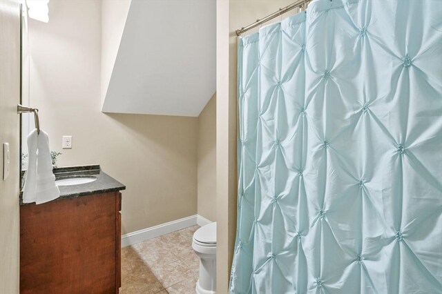 bathroom featuring vanity, tile patterned flooring, toilet, baseboards, and vaulted ceiling