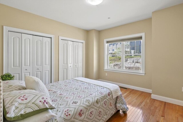 bedroom featuring baseboards, light wood finished floors, and two closets