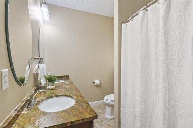 full bath featuring tile patterned flooring, double vanity, toilet, baseboards, and a sink