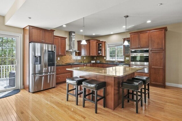 kitchen featuring light wood-style floors, wall chimney exhaust hood, a warming drawer, and stainless steel appliances