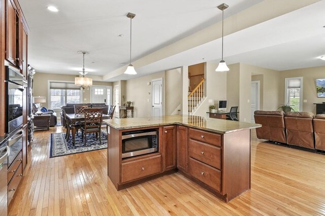 kitchen with light wood-style floors, open floor plan, light stone counters, appliances with stainless steel finishes, and decorative light fixtures