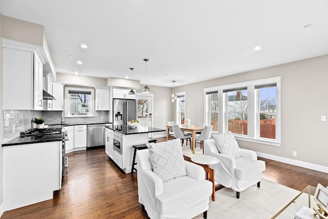 kitchen with a center island, backsplash, appliances with stainless steel finishes, decorative light fixtures, and white cabinetry