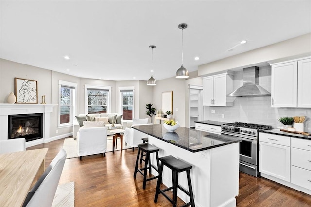 kitchen with decorative backsplash, high end stove, a kitchen island, wall chimney range hood, and white cabinetry