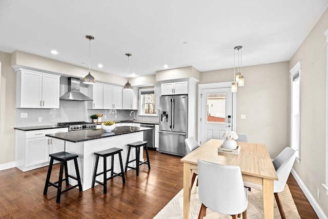 kitchen featuring decorative backsplash, appliances with stainless steel finishes, wall chimney exhaust hood, pendant lighting, and white cabinets