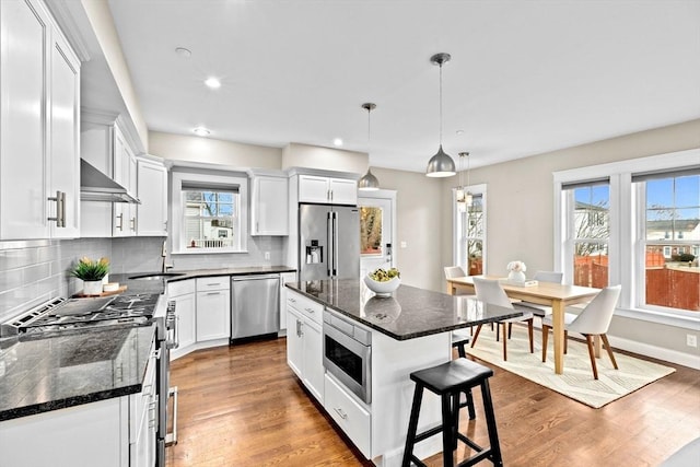 kitchen featuring premium appliances, decorative light fixtures, a kitchen island, and white cabinetry