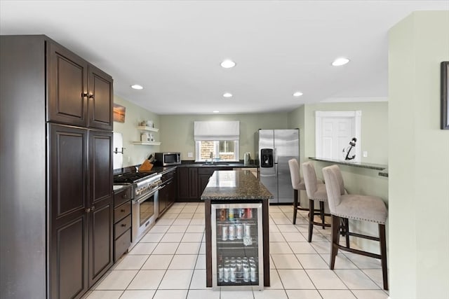 kitchen with stainless steel appliances, a kitchen island, a breakfast bar area, dark stone countertops, and beverage cooler