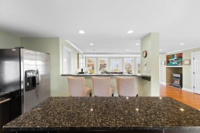 kitchen with kitchen peninsula, dark stone counters, hardwood / wood-style floors, crown molding, and stainless steel fridge